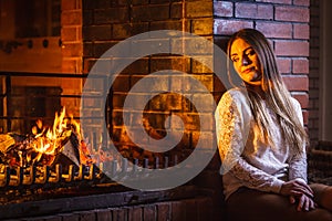 Pensive woman relaxing at fireplace. Winter home.