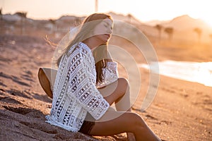Pensive woman sitting on the beach at sunset