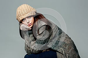 Pensive woman in warm winter outfit on gray background