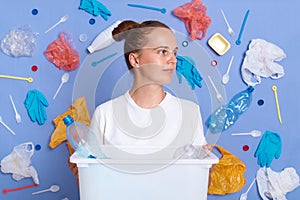 Pensive woman wearing white shirt isolated on blue wall with litter around holding can with rubbish, looking away, trash