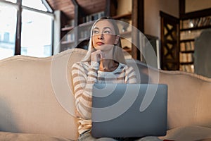 Pensive woman working on laptop at home