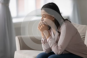 Pensive worried mixed race woman sitting on couch at home