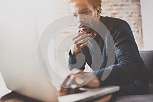 Pensive young African businessman using laptop while sitting on sofa at his modern coworking place.Concept of business