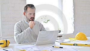 Pensive Young Architect Reading on Laptop in Office