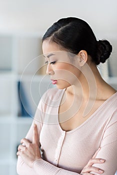 Pensive young asian woman standing with crossed arms and looking down