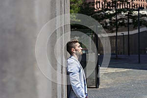 Pensive young bearded man looking away in the street while leaning on a wall outdoors