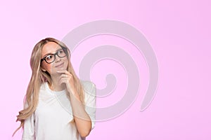 Pensive young blonde female in eyeglasses touching her chin, thinking, pondering and looking up, place for advertising or copy