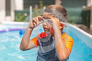 Pensive young boy with swim goggles looks away in a backyard pool photo