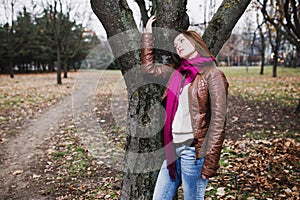 Pensive young brunette girl standing near tree