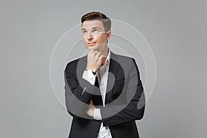 Pensive young business man in classic black suit shirt posing isolated on grey wall background. Achievement career