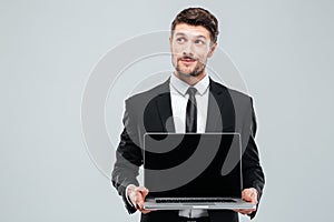 Pensive young businessman holding blank screen laptop and thinking