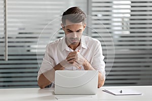 Pensive young businessman sitting at office, solving business challenge.