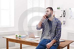 Pensive young businessman talking on mobile phone sits on the table