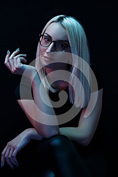 Pensive young Caucasian beautiful blonde woman with glasses . close-up portrait in neon light