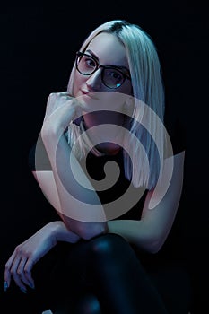 Pensive young Caucasian beautiful blonde woman with glasses . close-up portrait in neon light