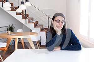 Pensive young caucasian woman with glasses feeling bored sitting at home office desk.