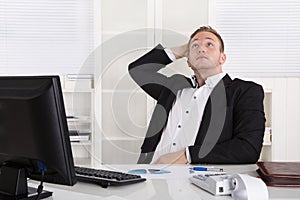 Pensive young dreaming businessman sitting at desk looking up.