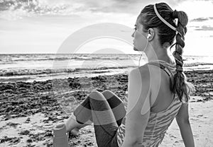 Pensive young fit woman on seashore relaxing after workout