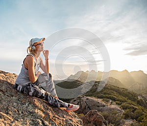 Pensive young girl in headphones enjoying beautiful sunset on the top of a mountain