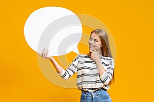 Pensive young girl holding blank speech bubble over yellow background