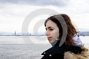 Pensive young girl looking to the sea from boat. Teenager girl at ferryboat. Cold grey sea