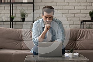 Pensive young male working at home focused on computer screen