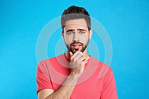 Pensive young man on blue background. Thinking about difficult question