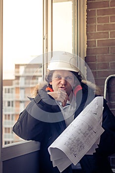 Pensive young man builder in hard hat standng and thinking. Soft focus, toned.
