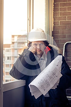 Pensive young man builder in hard hat standng and thinking. Soft focus, toned.