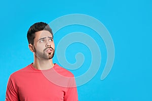 Pensive young man on light blue background, space for text. Thinking about difficult question