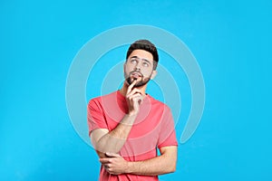 Pensive young man on light blue background. Thinking about difficult question