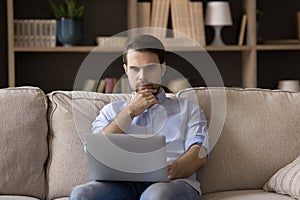 Pensive young man working on computer at home.