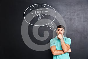 Pensive young man standing and thinking over chalkboard background