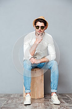 Pensive young man in sunglasses sitting and thinking