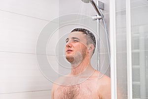 Pensive young man taking a shower in the bathroom