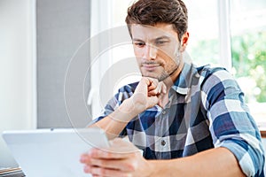 Pensive young man thinking and using tablet at home