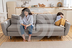 Pensive young mommy sitting on couch with offended after family quarrel and mom scolding son