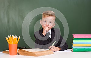 Pensive young student in black suit near empty green chalkboard