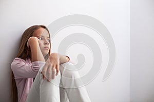 Pensive young teenager girl sitting by the wall on the floor