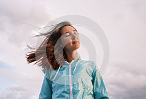 Pensive young woman with closed eyes in the cloudy sky background.