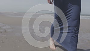 Pensive young woman in denim jacket walking on lonely beach.