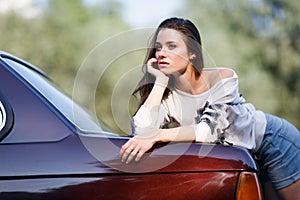 Pensive young woman leaned on the hood of her car