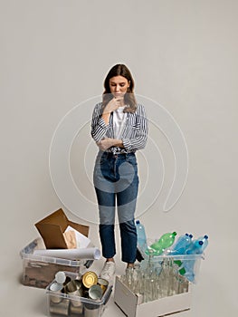 Pensive Young Woman Looking At Containers With Sorted Waste Arround Her