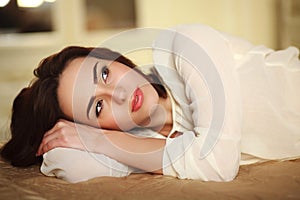 Pensive young woman lying on the bed at home