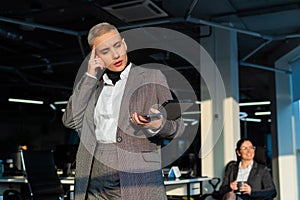 Pensive young woman with short hair uses mobile phone in office.
