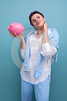 a pensive young woman with a short haircut holds a piggy bank and thinks where to invest the accumulated money