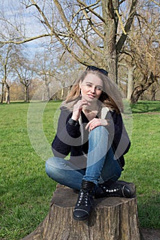 Pensive young woman sitting on an old tree stump