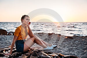 pensive young woman sitting on plaid at beautiful sea coast