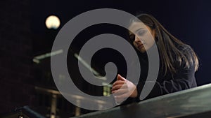 Pensive young woman standing on night city street and thinking about life