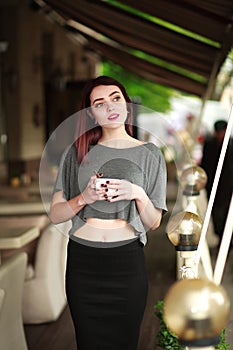 Pensive young woman in summer cafe with cup of coffee